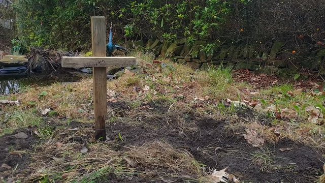 A cross impaled in the grounds of a family garden, remembering a loved one with a beautiful backdrop and pond.