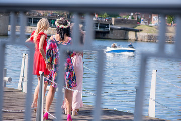 Girls in luxury, colorful dresses standing on wooden footbridge and patiently waiting for sailors...