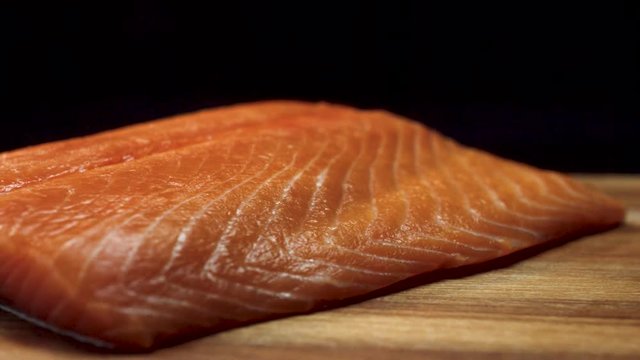 Close-up of juicy piece of salmon. Juicy fresh and red slice of salmon meat lying on wooden board on black background