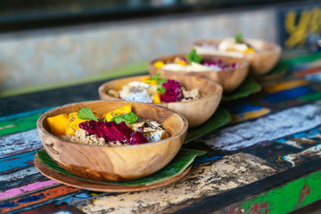 Close up four smoothies bowls made with mango, banana, granola, grated coconut, dragon fruit, chia seeds and mint on colored background