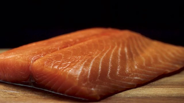 Close-up of juicy piece of salmon. Juicy fresh and red slice of salmon meat lying on wooden board on black background