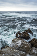 Ocean waves crashing on rocks, coastline view in California. Sand and rocks on a beach