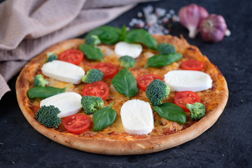 Italian pizza with Mozzarella cheese, tomatoes, broccoli, Spices and fresh basil. Pizza and kitchen napkin near, on black stone background