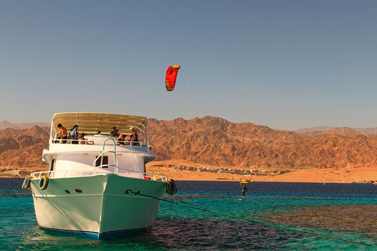 Dahab, Egypt-JANUARY 06, 2019: Kiteboarder enjoying surfing in blue water near the moored yacht. Travel and tourism concept. Red Sea, Sinai Peninsula of Egypt