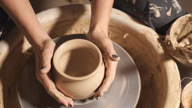 Woman girl her hands dub wall jug, sculpts out of clay on circle, top view