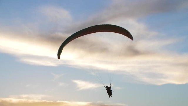 Silhouette of paraglider flying across golden sunset