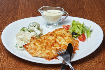 pork chops baked in cheese, broccoli, cherry tomatoes, lettuce, olives and sour cream, served on a white plate