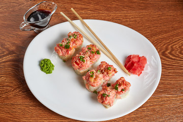 rolls with chili pepper, red caviar, sesame, green onions, lie on a plate with wasabi, ginger and chopsticks, standing next to soy sauce