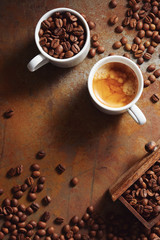 Cup of espresso with coffee beans scattered over a rustic surface.
