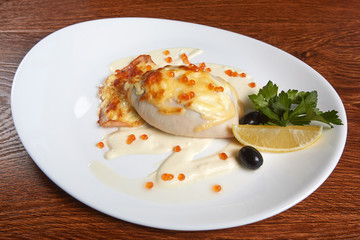 squid stuffed with cheese and baked flounder, decorated with white sauce and red caviar, next to a slice of lemon, coriander and black olives