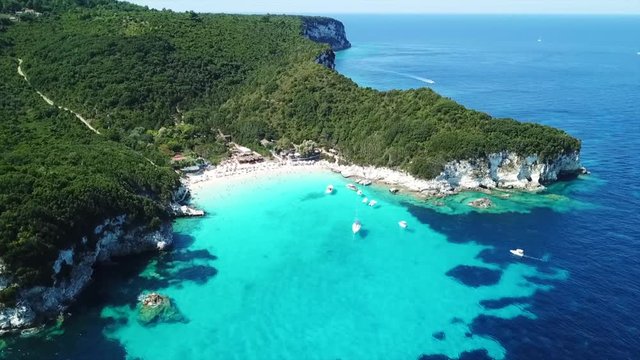 Aerial drone video of tropical paradise turquoise beach of Voutoumi with sail boats docked in island of Antipaxos, Ionian, Greece