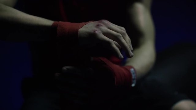 Close-up of boxer's hand. Close-up boxer ties injured hands with red ribbon in dark locker room, preparing for training