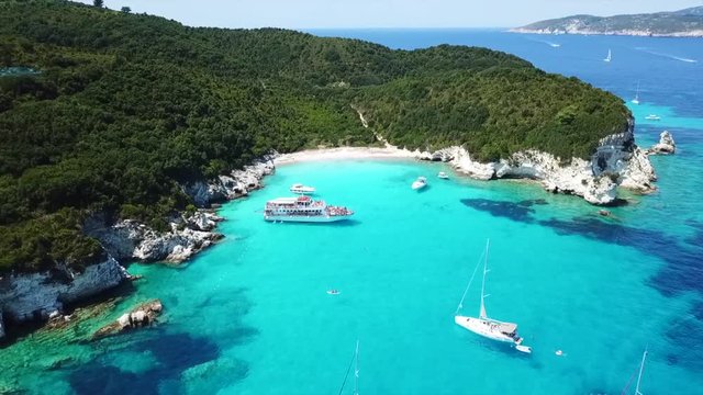 Aerial drone video of tropical paradise turquoise beach of Voutoumi with sail boats docked in island of Antipaxos, Ionian, Greece