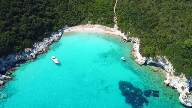 Aerial drone video of tropical paradise turquoise beach of Voutoumi with sail boats docked in island of Antipaxos, Ionian, Greece