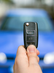 A person holding car key (remote control) in hands on blur blue car background.