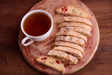 Delicious biscotti cookies with dried cherries and hazelnuts with black tea and white cup. Organic style. White cup of tea.