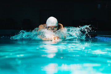 Professional woman swimmer swim using breaststroke technique on the dark background - obrazy, fototapety, plakaty