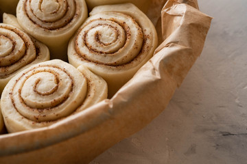 Raw cinnamon rolls in baking plate on kitchen table. Copy space.