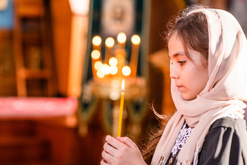 Little girl with a candle prays in the church near the icon