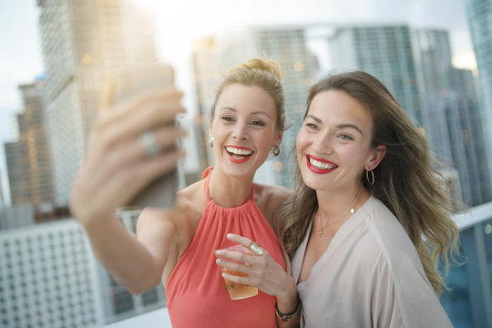 Two Attractive Funloving Friends Taking Selfie On Night Out At Roofttop Bar In City