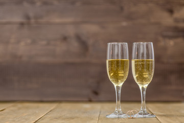 Pair glass of champagne with golden wedding rings on wooden background. Empty space for your text