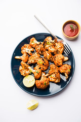 Tandoori Gobi / Roasted cauliflower Tikka is a dry dish made by roasting Cauliflowers in Oven/Tandoor. It's  popular starter food from India. served with ketchup. selective focus