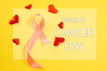 The text world cancer day and a pink ribbon on a yellow background. The cancer, health, breast, awareness, campaign, disease, help, care, support, hope, illness, survivor and healthcare concept