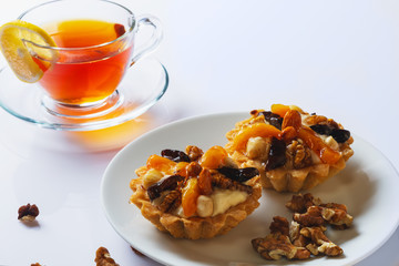 Basket-cake with nuts, dried fruits and jelly on white plate. Cup of tea. Closeup. Selective focus.