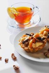 Basket-cake with nuts, dried fruits and jelly on white plate. Cup of tea. Closeup. Selective focus.