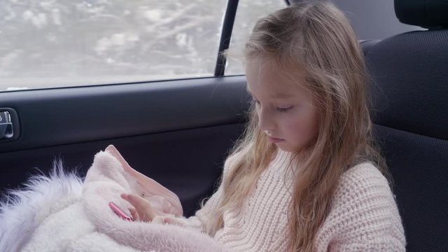 Young adorable girl surf internet while travel in back sits car at smartphone. Winter travel vacation. White caucasian girl with long hair. Read information on cell phone. Travel concept
