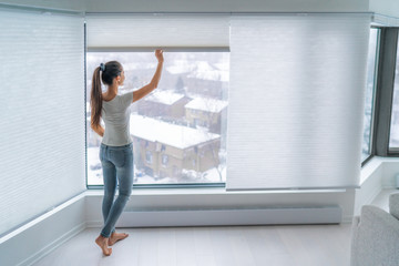 Woman closing cellular shades on apartment window keeping energy and heat indoors with honeycomb blind curtain. Cordless pleated shades in modern home living lifestyle. Interior decor design. - obrazy, fototapety, plakaty