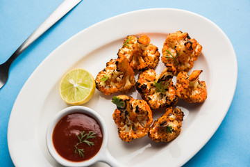 Tandoori Gobi / Roasted cauliflower Tikka is a dry dish made by roasting Cauliflowers in Oven/Tandoor. It's  popular starter food from India. served with ketchup. selective focus