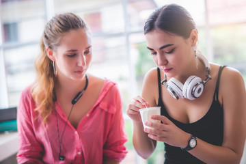 Two happy young attractive Caucasian women talking together and using smartphone or cellphone at coffee or coffe shop in the morning 