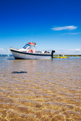 Obraz premium White boat on sand surrounded with water and rocks in summertime in Noirmoutier