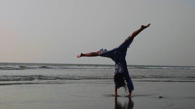 Young gymnast woman doing handspring on sandy beach
