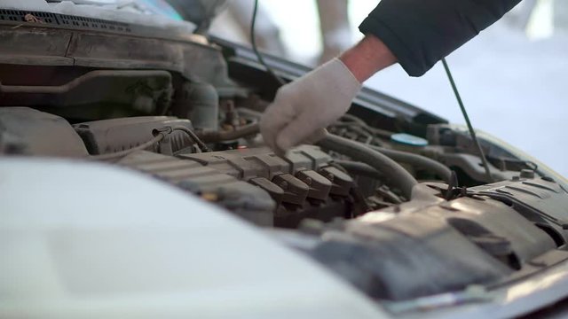 A man checks the engine of his car. It is very cold outside.