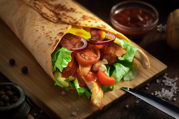 Shawarma sandwich on wooden rustic background. Gyro fresh roll with pita with grilled chicke, lettuce salad, bacon, tomato, sauces, cheese and vegetables. Tasty shawarma - middle eastern snack. - obrazy, fototapety, plakaty