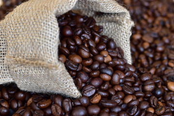 Small jute bag of coffee on the background of fresh aromatic beans of roasted coffee close up