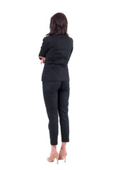 Back view of business woman in black suit with crossed arms watching interested. Full body isolated on white background. 