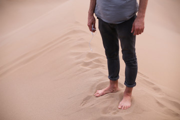 Man with earphones in his hand is standing barefoot on a top of a sand hill in big beautiful orange desert sand dunes in Yazd, Iran