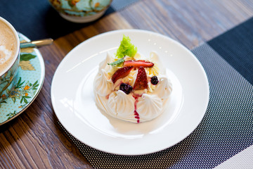 Cup cappucino with heart coffee art a light and airy pavlova's dessert with merengue and fruit