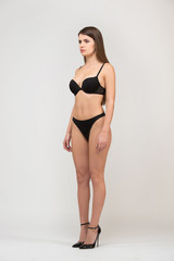 Fototapeta premium Full length portrait three-quarter of beautiful brunette women with slim figure in black bra and shorts. Model snaps in the studio on white background