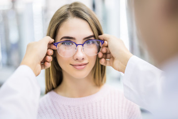 Beautiful smiling woman choosing eyeglasses while male oculist standing near with another...