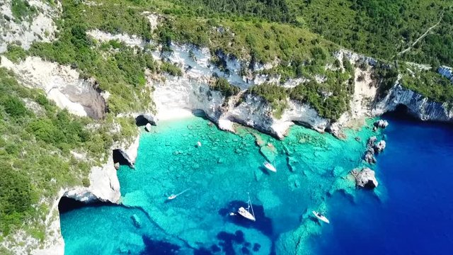 Aerial bird's eye view video taken by drone of caves  and boats docked in caribbean tropical beach with turquoise - sapphire waters and caves forming a blue lagoon