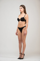 Fototapeta premium Full length portrait three-quarter of beautiful brunette women with slim figure in black bra and shorts. Model snaps in the studio on white background