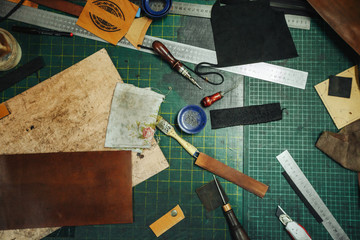 Leatherworking tools. Riveter, awl, ruler, pliers, tassels, pencil, leather pieces, rivets and fasteners are on the table. Close up photo.