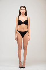 Fototapeta premium Front view full length portrait of beautiful brunette women with slim figure in black bra and shorts. Model snaps in the studio on white background