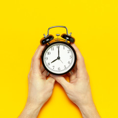 Flat lay top view male hand holding black vintage alarm clock on bright yellow color background...