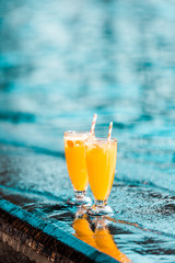 orange cocktails with straws standing near swimming pool