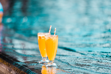 two orange cocktails glasses with straws standing at poolside